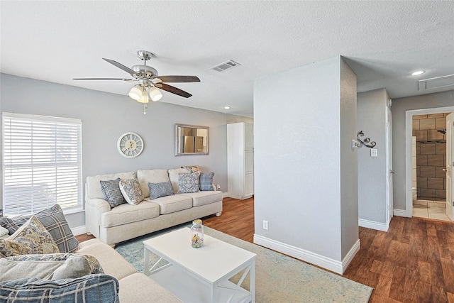 living room featuring dark wood-type flooring, ceiling fan, and a textured ceiling