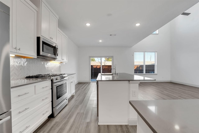 1004 Emil Pl, Allen, TX 75013 - kitchen featuring appliances with stainless steel finishes, light wood-style flooring, decorative backsplash, white cabinetry, and a center island