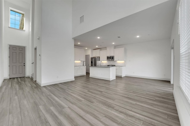 unfurnished living room with light hardwood / wood-style floors and a high ceiling