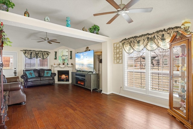 living room with lofted ceiling, a lit fireplace, ceiling fan, and dark wood-style floors