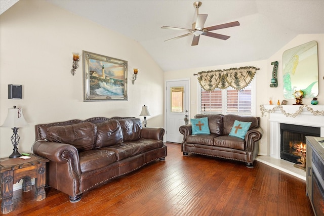 living room with lofted ceiling, dark wood-type flooring, a warm lit fireplace, and a ceiling fan