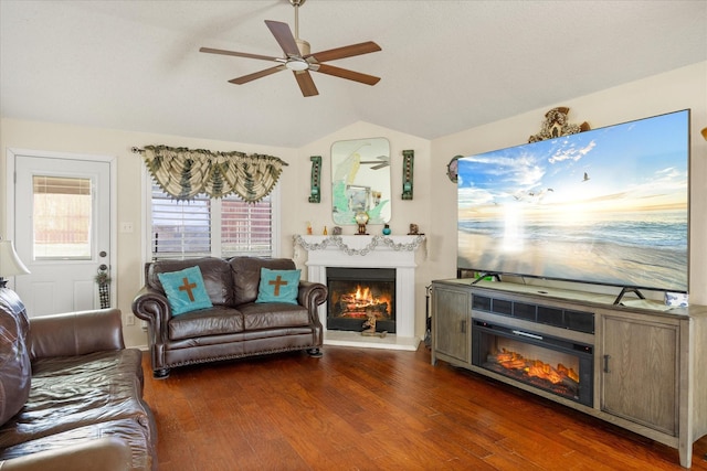 living room with ceiling fan, a lit fireplace, vaulted ceiling, and dark wood finished floors