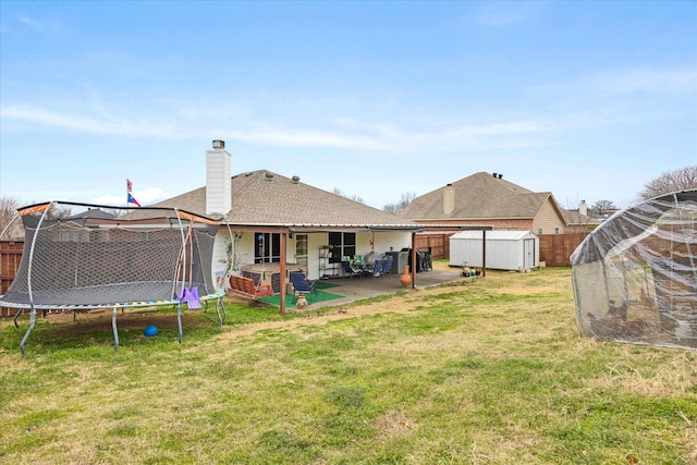 rear view of property featuring a patio, a chimney, a trampoline, an outdoor structure, and a shed