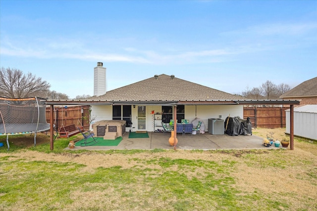 back of property featuring a fenced backyard, a chimney, a trampoline, a yard, and a patio area