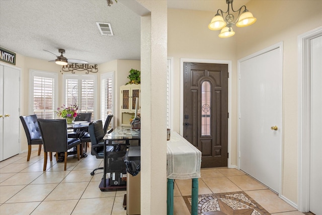 foyer entrance with light tile patterned floors, visible vents, a textured ceiling, and ceiling fan with notable chandelier