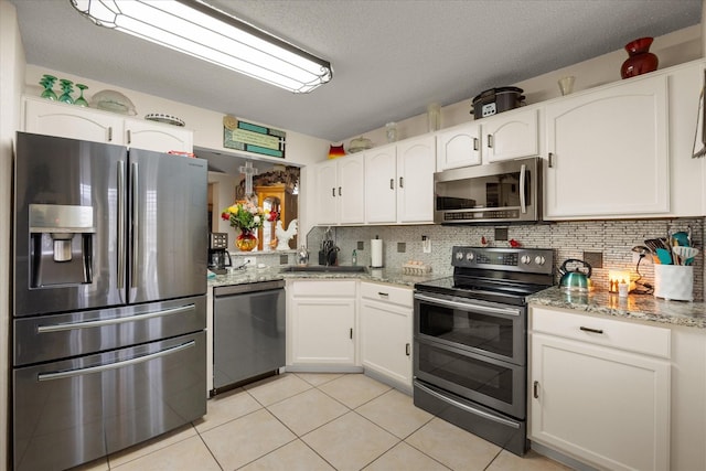 kitchen featuring stainless steel appliances, white cabinetry, light stone counters, and tasteful backsplash