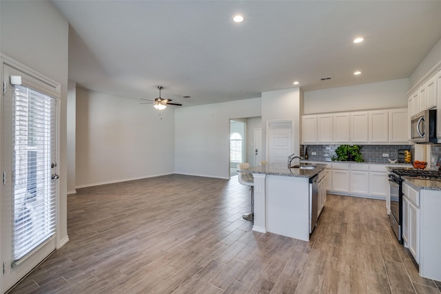 kitchen with stainless steel appliances, dark stone countertops, a kitchen island with sink, and white cabinets