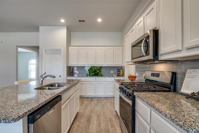 kitchen with a center island with sink, visible vents, appliances with stainless steel finishes, white cabinetry, and a sink