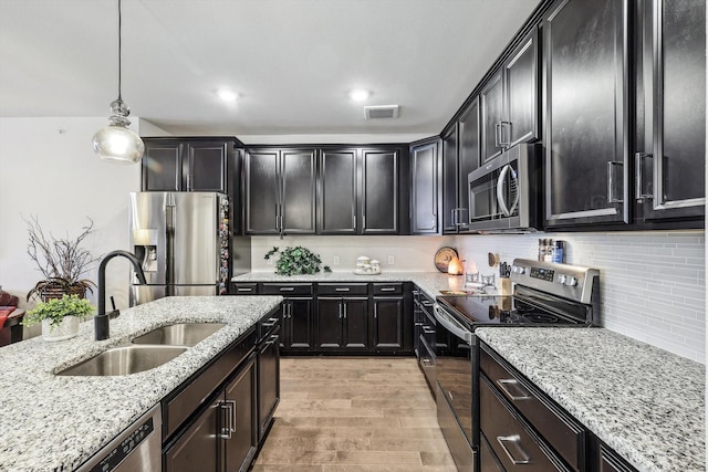 kitchen with tasteful backsplash, sink, hanging light fixtures, stainless steel appliances, and light stone countertops