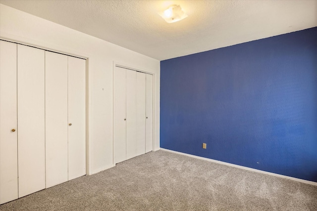 unfurnished bedroom featuring a textured ceiling, carpet flooring, and two closets