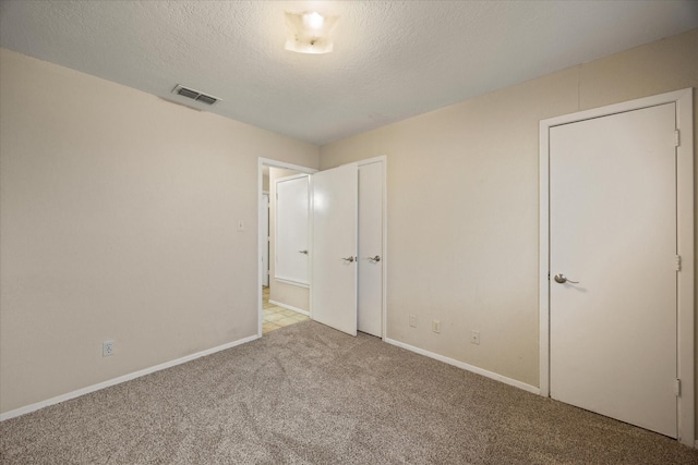 unfurnished bedroom featuring carpet, visible vents, a textured ceiling, and baseboards