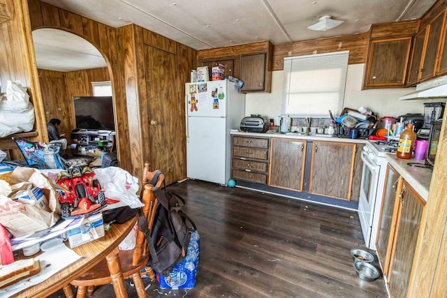 kitchen with dark wood-type flooring, white appliances, and wood walls