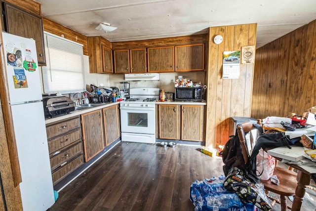 kitchen with white appliances, dark hardwood / wood-style flooring, wood walls, and sink