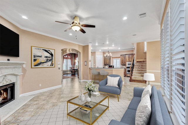 living room with a premium fireplace, ornamental molding, and ceiling fan with notable chandelier