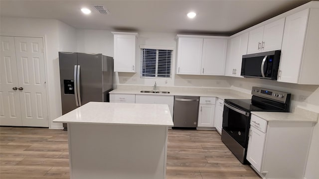 kitchen with appliances with stainless steel finishes, white cabinetry, sink, a center island, and light hardwood / wood-style floors