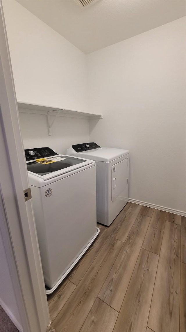 clothes washing area with washing machine and dryer and light hardwood / wood-style flooring