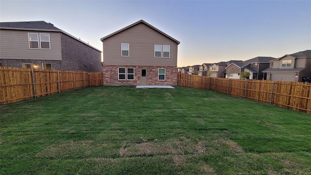 back house at dusk featuring a patio and a lawn