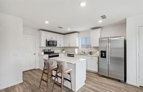 kitchen featuring appliances with stainless steel finishes, a breakfast bar area, white cabinets, and light hardwood / wood-style floors