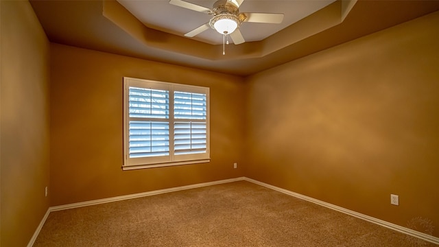 empty room featuring ceiling fan, a raised ceiling, and carpet