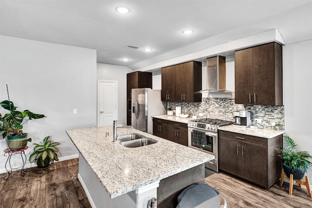 kitchen featuring appliances with stainless steel finishes, sink, decorative backsplash, a center island with sink, and wall chimney exhaust hood