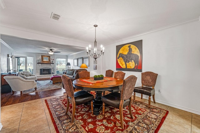 tiled dining area with crown molding, a fireplace, and ceiling fan with notable chandelier