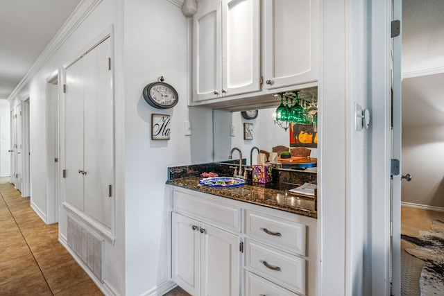 bar with sink, light tile patterned floors, white cabinetry, dark stone countertops, and ornamental molding