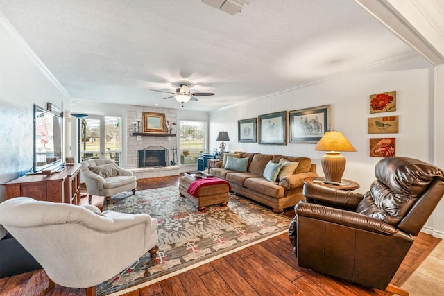 living room with dark wood-type flooring, ceiling fan, ornamental molding, a textured ceiling, and a stone fireplace