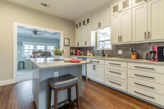 kitchen featuring visible vents, a kitchen island, glass insert cabinets, white cabinetry, and a sink