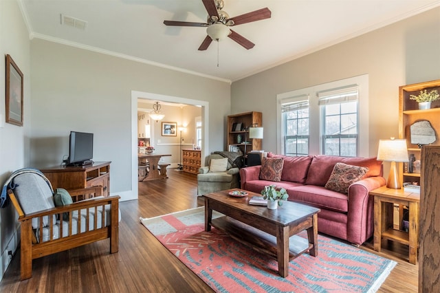 living area with a ceiling fan, wood finished floors, visible vents, and crown molding