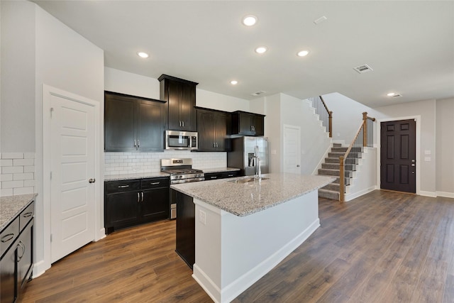 kitchen featuring sink, light stone counters, a center island with sink, appliances with stainless steel finishes, and dark hardwood / wood-style floors