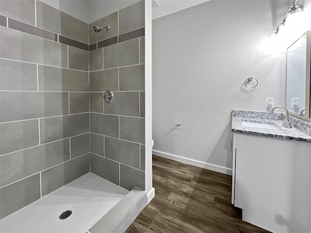 full bathroom with baseboards, wood finished floors, vanity, and a tile shower