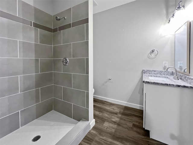 bathroom featuring baseboards, wood finished floors, vanity, and a tile shower