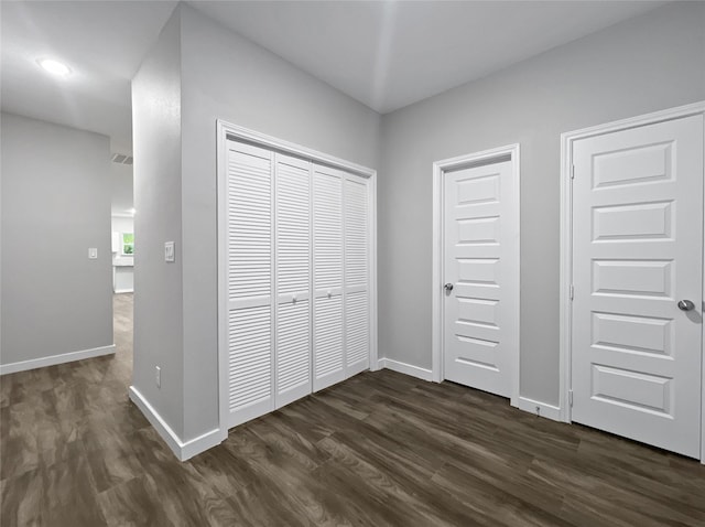 unfurnished bedroom featuring a closet, baseboards, and dark wood-type flooring