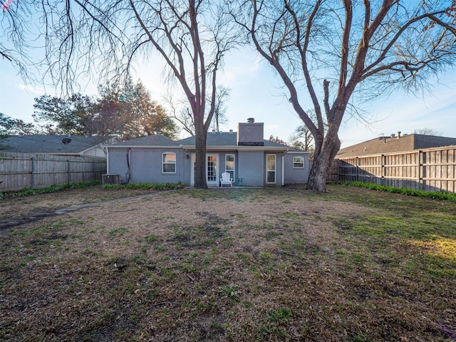 back of house with a yard, a chimney, a fenced backyard, and central air condition unit