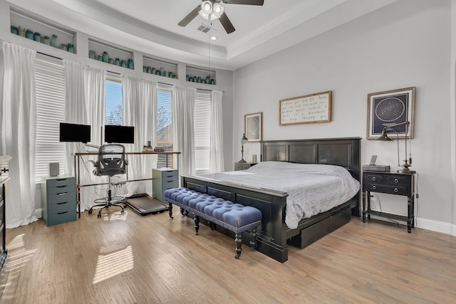 bedroom with a raised ceiling, light wood-style floors, ornamental molding, and visible vents