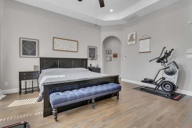 bedroom featuring baseboards, visible vents, a tray ceiling, arched walkways, and wood finished floors