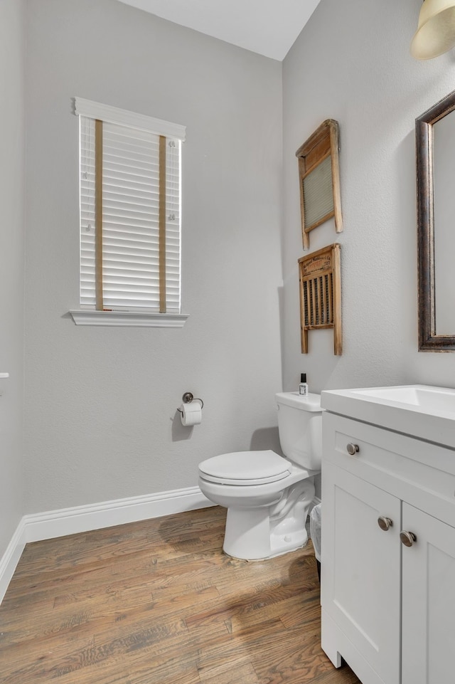 half bathroom with toilet, vanity, wood finished floors, and baseboards