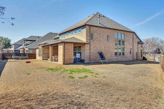 back of house featuring brick siding, a fenced backyard, a trampoline, and a shingled roof