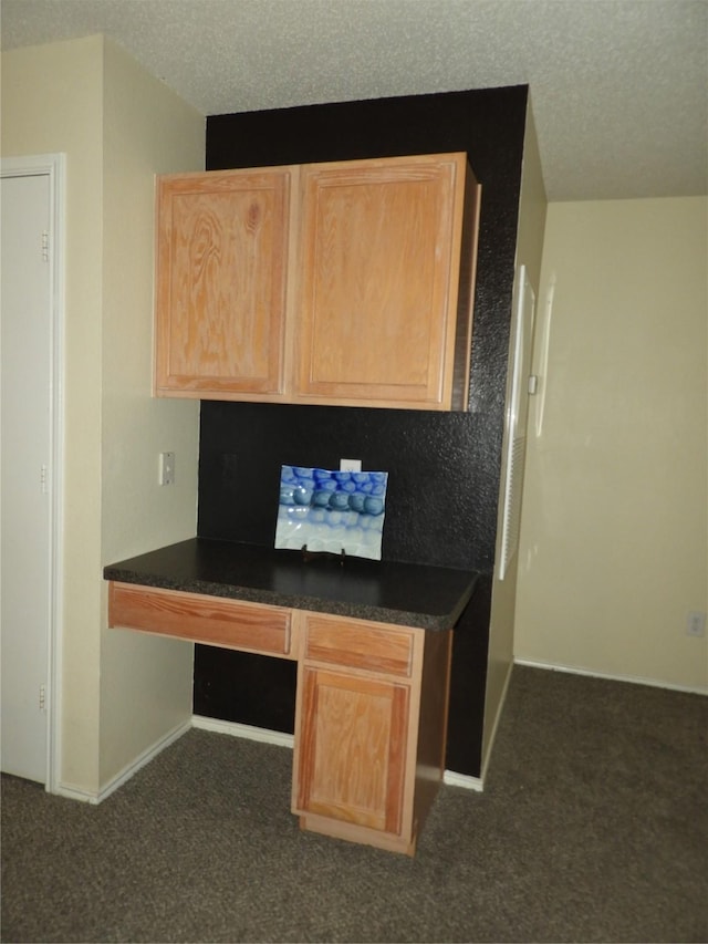 unfurnished office featuring dark carpet, built in desk, and a textured ceiling