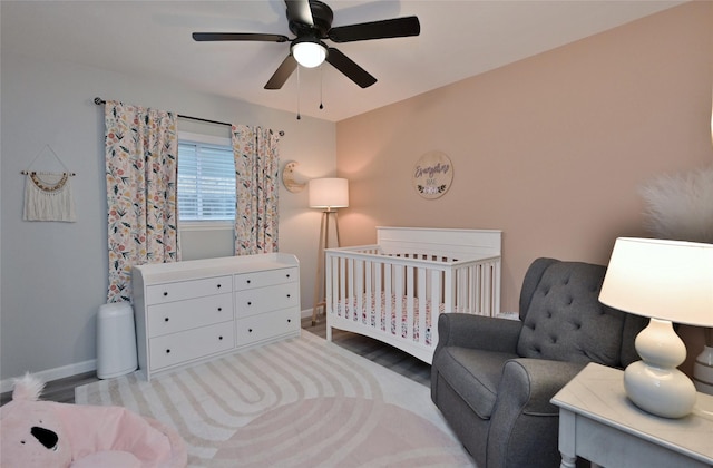 bedroom with a crib, ceiling fan, and light hardwood / wood-style floors