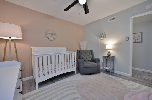 bedroom with a nursery area, ceiling fan, and light hardwood / wood-style flooring