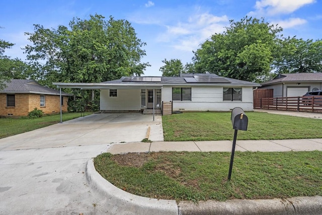 ranch-style home featuring solar panels, concrete driveway, a front yard, fence, and an attached carport