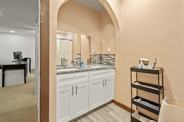 bathroom featuring wood finished floors, double vanity, tasteful backsplash, and a sink