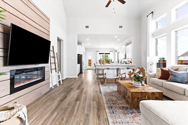 living room featuring a towering ceiling, ceiling fan, and light hardwood / wood-style flooring