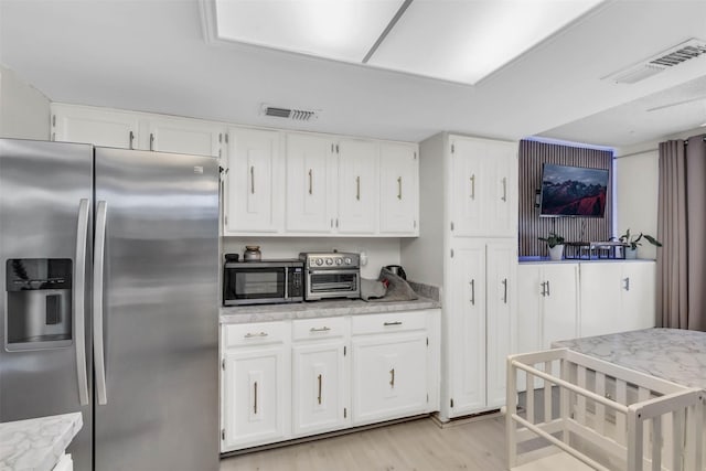 kitchen featuring appliances with stainless steel finishes, light stone counters, white cabinets, and light wood-type flooring