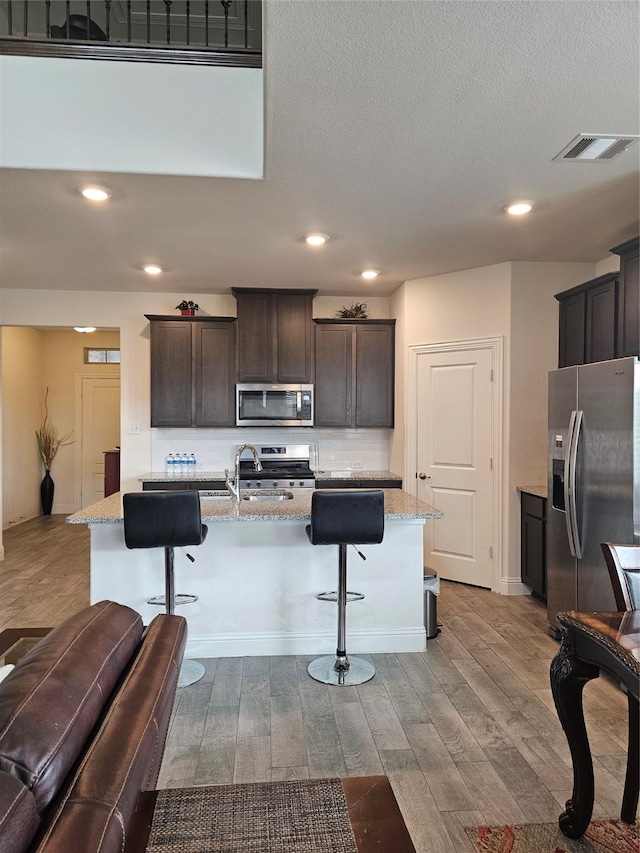 kitchen featuring stainless steel appliances, a kitchen breakfast bar, light stone countertops, and an island with sink