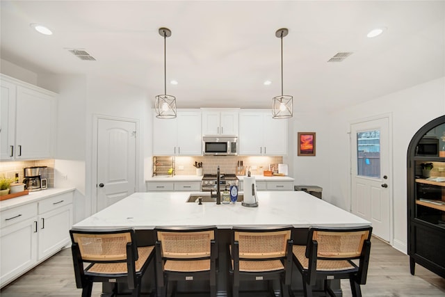 kitchen featuring pendant lighting, stainless steel appliances, a kitchen island with sink, and white cabinets