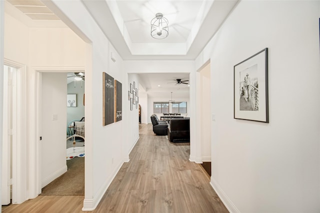 corridor with light wood-type flooring and a tray ceiling