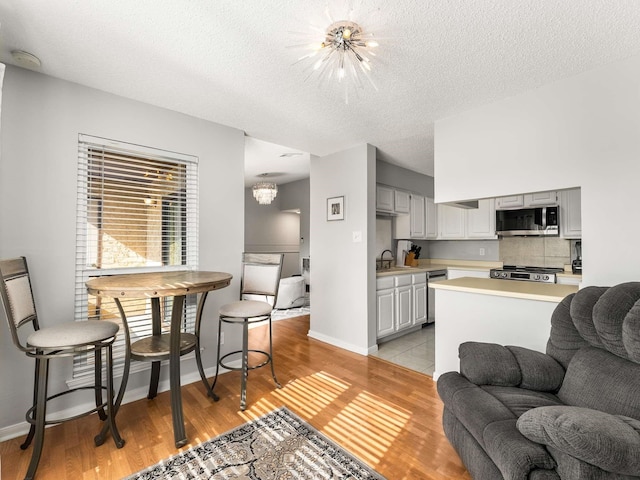 interior space featuring appliances with stainless steel finishes, light hardwood / wood-style flooring, a textured ceiling, sink, and an inviting chandelier