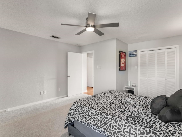 bedroom featuring ceiling fan, a closet, light carpet, and a textured ceiling